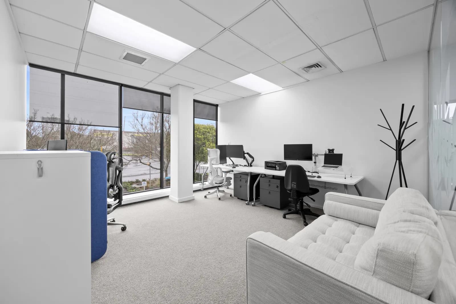 Furnished private office with desks, seating, and large windows
